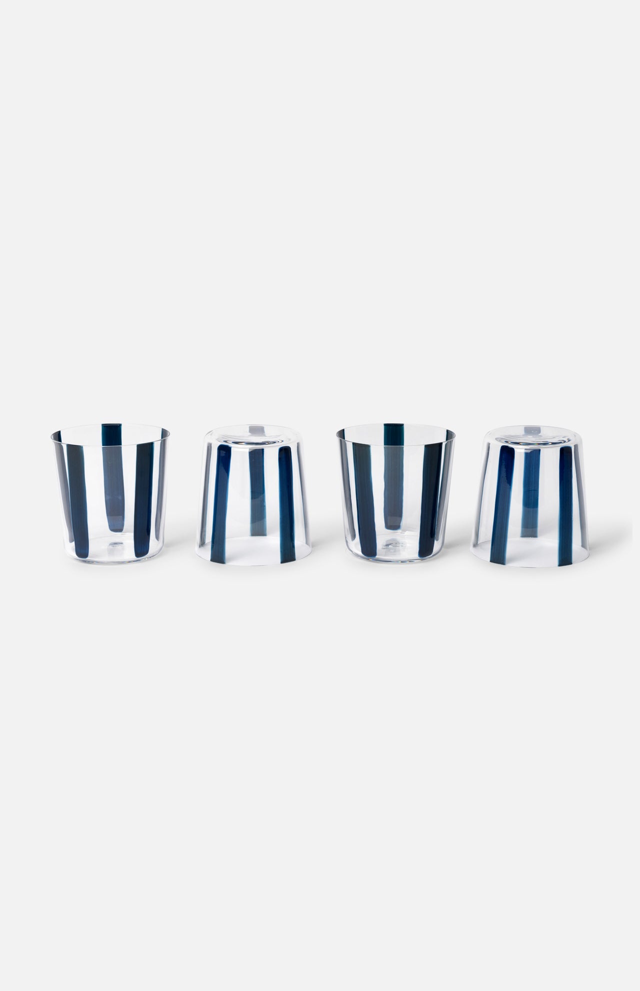 The CONRAN SHOP Nova Stripe Tumbler Set of 4 features clear crystal glasses with vertical blue stripes, stylishly arranged upright and upside down against a white background—perfect for your hand-painted glassware collection.