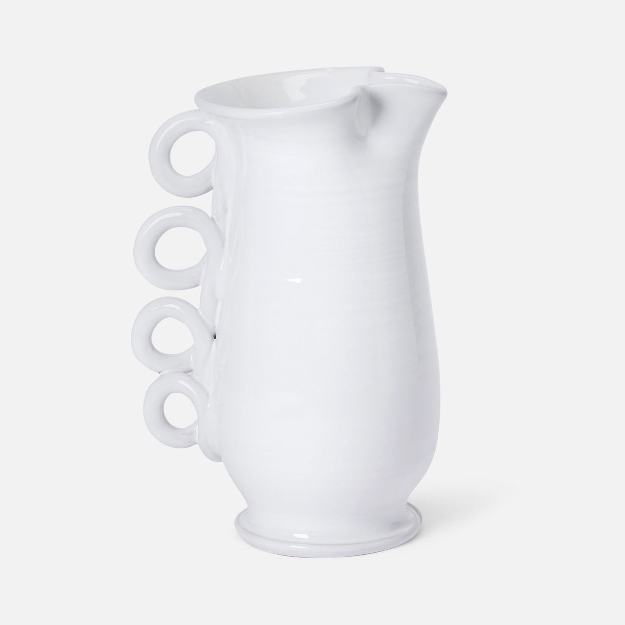 The Puglia Jug with Ring Handle by THE CONRAN SHOP is a white ceramic pitcher inspired by Puglia ceramics, featuring a curved body and four ring handles stacked vertically on one side.