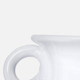 Close-up of THE CONRAN SHOP's Puglia Jug with Ring Handle, a glossy white ceramic piece inspired by traditional handcrafted Puglia ceramics. Only part of the jug and its round handle are visible against a plain light gray background.