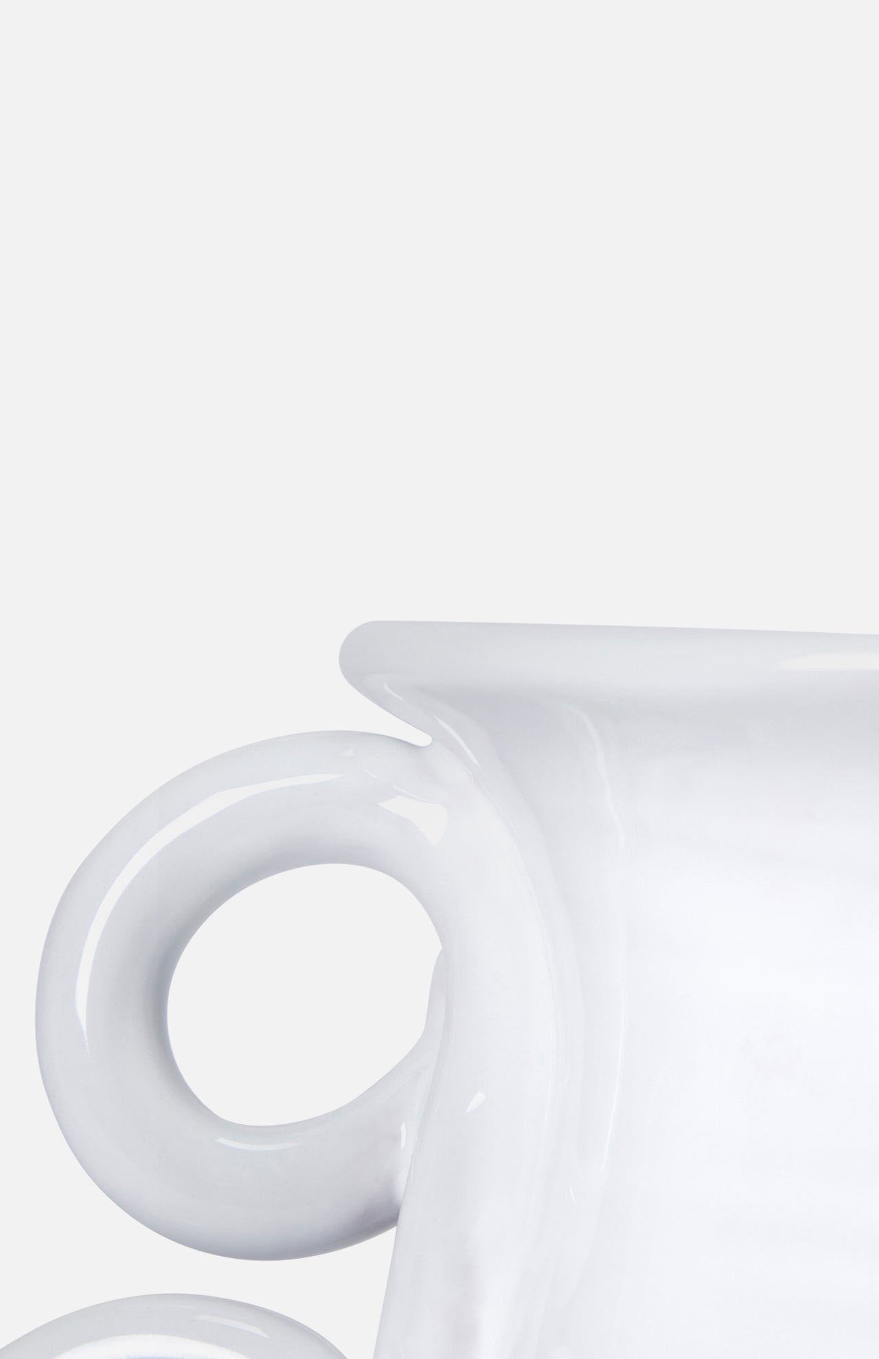 Close-up of THE CONRAN SHOP's Puglia Jug with Ring Handle, a glossy white ceramic piece inspired by traditional handcrafted Puglia ceramics. Only part of the jug and its round handle are visible against a plain light gray background.