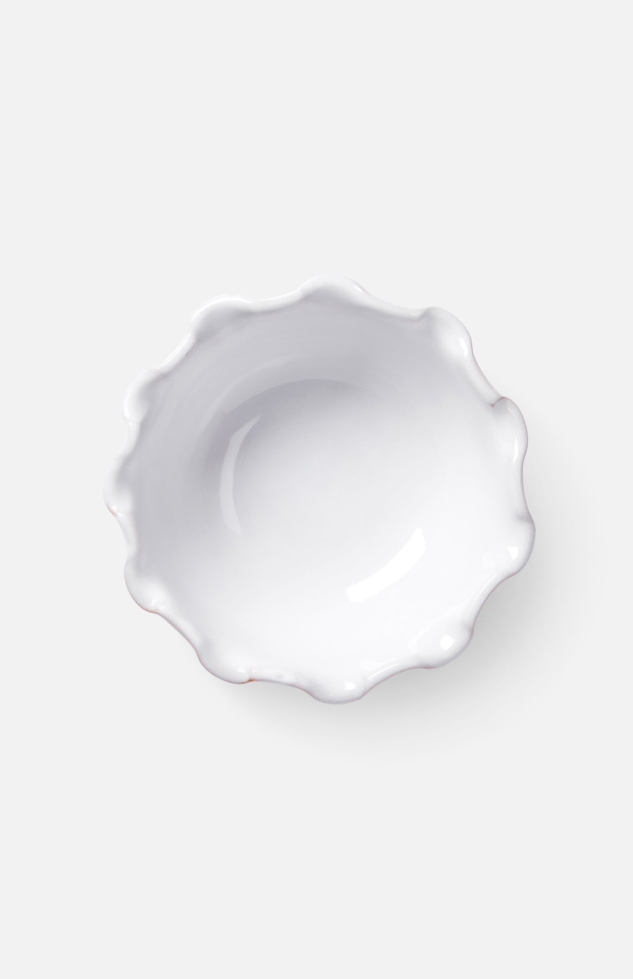 The Puglia Scalloped Small Bowl by THE CONRAN SHOP is a white stoneware piece with a glossy finish and wavy edges, shown from above on a light gray background. Handcrafted in Italy, it offers timeless elegance.