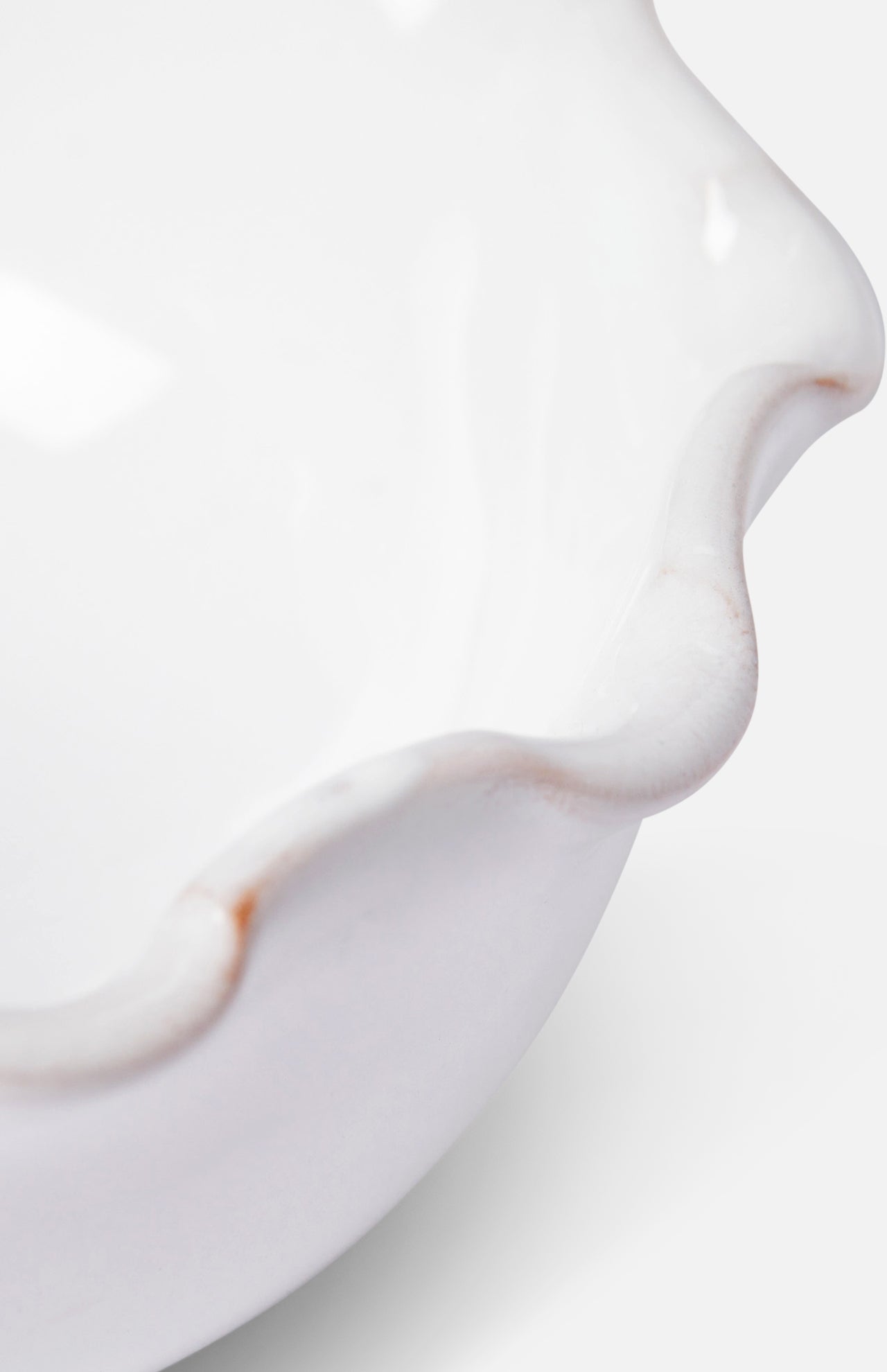 Close-up of the rim of THE CONRAN SHOP's Puglia Scalloped Small Bowl, a white stoneware piece with scalloped edges and subtle brown accents that highlight its handcrafted Italian artistry.