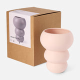 A sculptural, pale pink Stacked Spheres Vase Plaster by THE CONRAN SHOP with rounded, bubble-like shapes sits beside its brown box, which features an image and description of the vase on a white label.