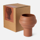 The Tree Vase Cocao by THE CONRAN SHOP, a matte terracotta-hued earthenware piece with a sculptural, rounded form, is displayed beside its brown box featuring the vase’s image and product details on the label.