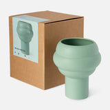 The CONRAN SHOP's Tree Vase Sage Green features a modern matte finish and layered rounded design, shown beside its brown cardboard box displaying an image and label of the earthenware vase on the front.