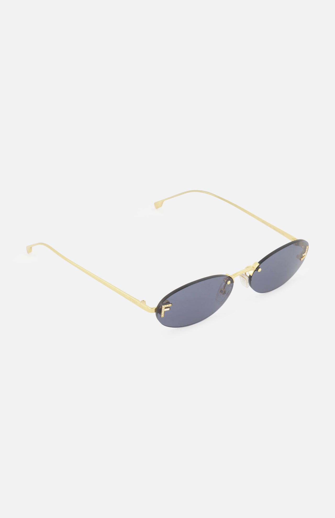 The FENDI Oval Gold Sunglasses are gold-framed, rimless statement sunglasses with subtle gold Fendi lettering and oval dark lenses, showcased from an angle against a plain white background.