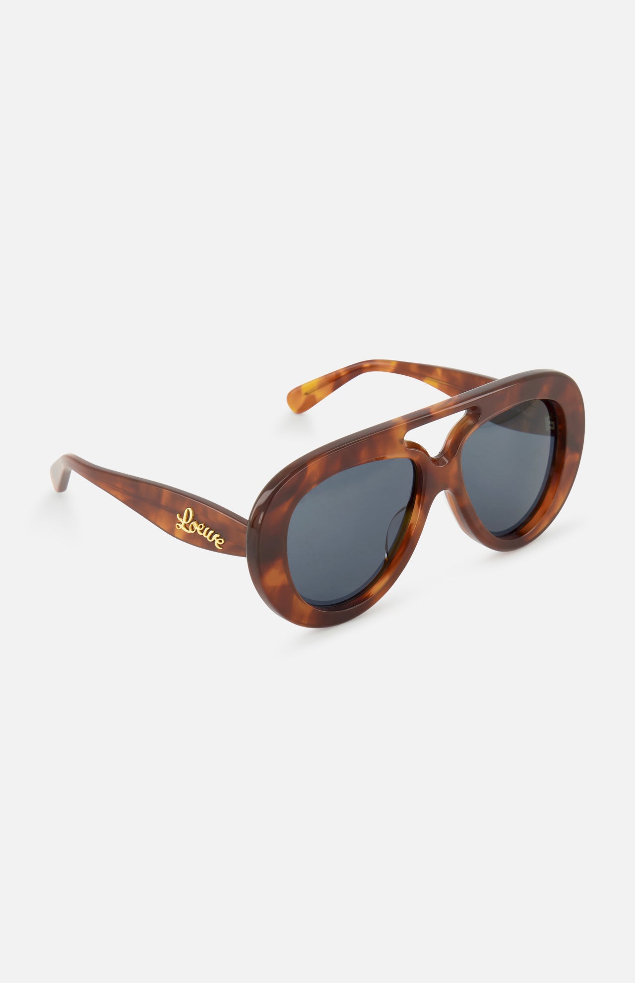 The Loewe Aviator Brown Tortoiseshell Sunglasses by LOEWE feature modern oval frames with dark lenses and a gold LOEWE logo on the left temple, elegantly showcased against a white background.