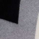 A close-up of three overlapping fuzzy fabric swatches in black, gray, and off-white—showcasing the soft texture featured in THEORY’s Cashmere Chevron Yoke Sweater.