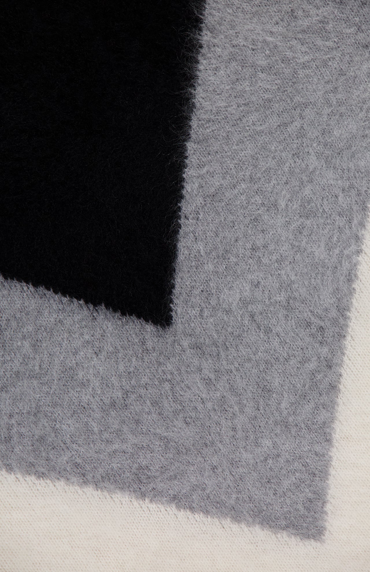 A close-up of three overlapping fuzzy fabric swatches in black, gray, and off-white—showcasing the soft texture featured in THEORY’s Cashmere Chevron Yoke Sweater.