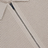 Close-up of THE­ORY's Gary Zip Sweater Jacket in beige waffle-knit cotton-cashmere, featuring a center zipper, folded collar, and a partially visible black label with white text at the top.