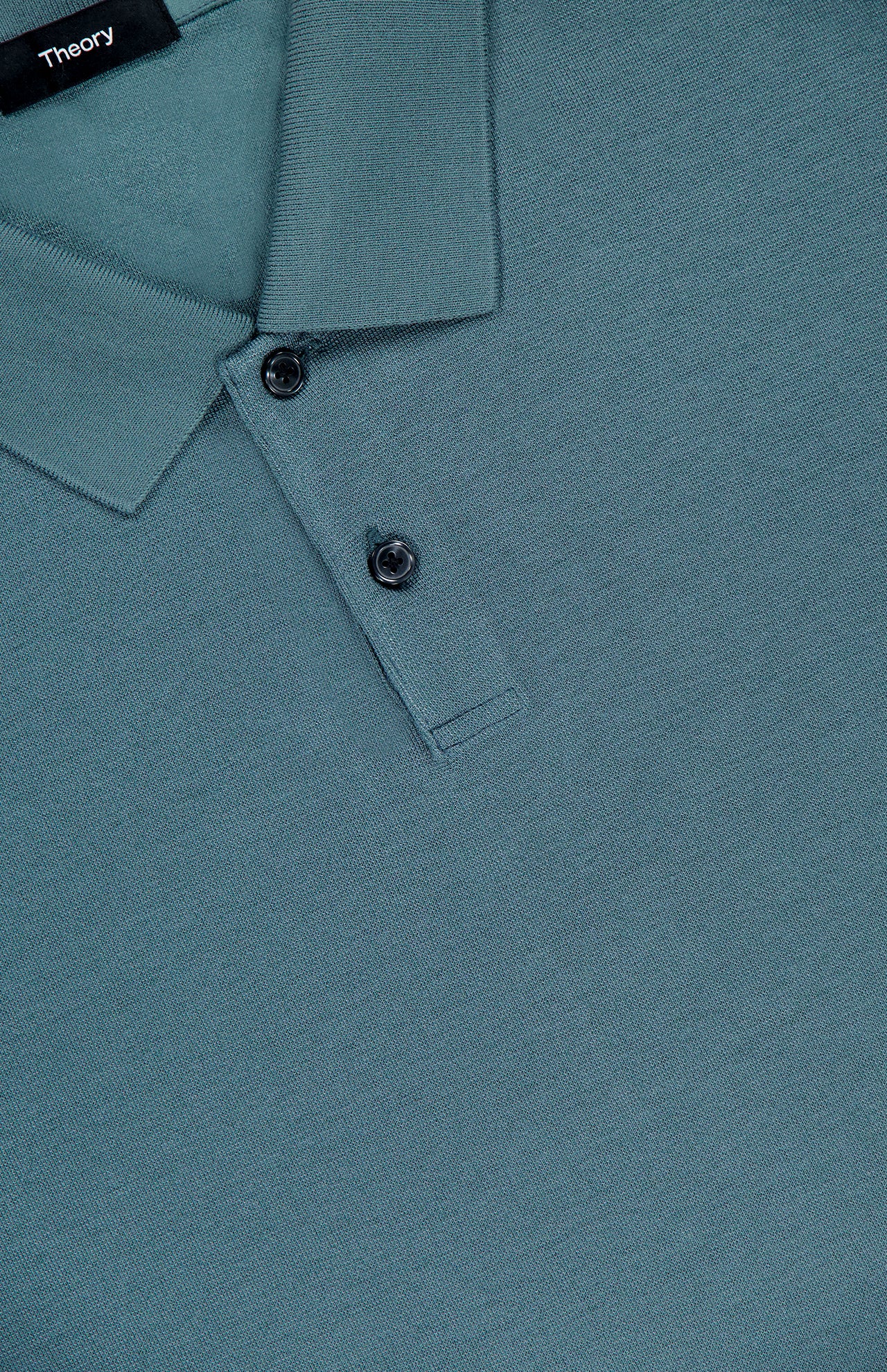 Close-up of the THEORY Goris Long Sleeve Polo Shirt in teal, made from lightweight stretch jersey with a collar and two black buttons. The Theory brand label is partially visible at the top left.