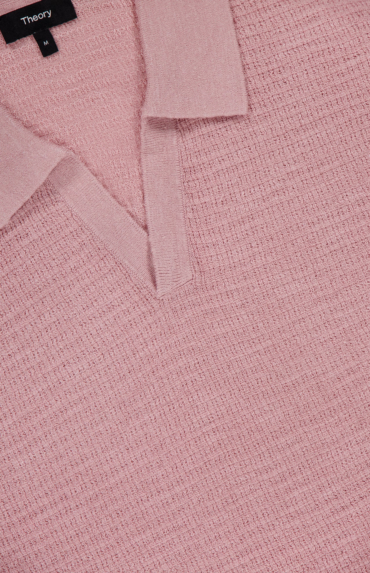 Close-up of the Brenan Knit Johnny Collar Polo Shirt by THEORY in light pink, featuring a textured knit and V-neck Johnny collar with an open neckline displaying the black THEORY label.