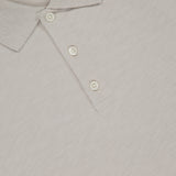Close-up of the THEORY Bron Cosmos Polo Shirt in light beige, featuring three white buttons, a ribbed collar, and a partially visible Theory tag at the top.