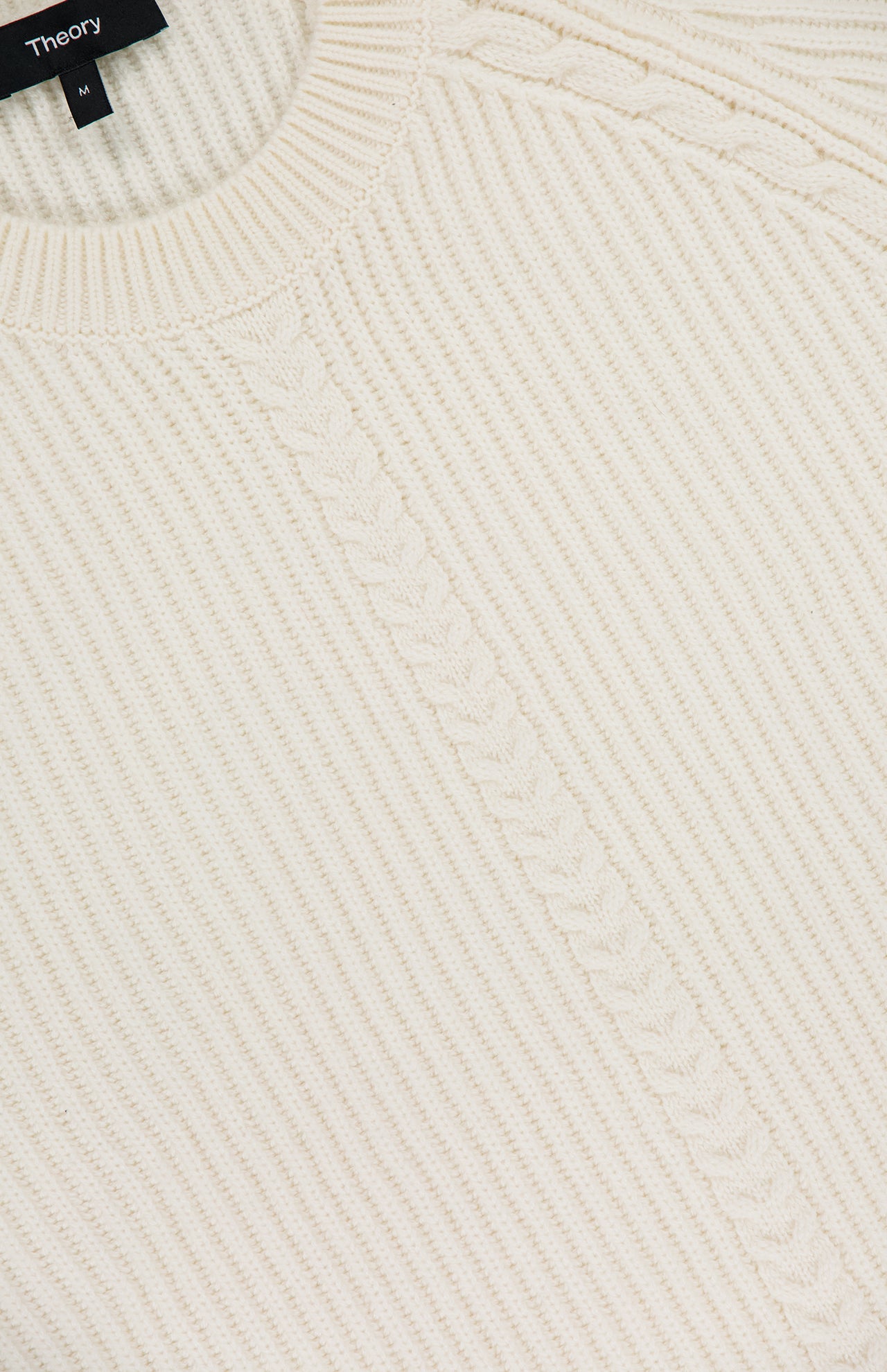 Close-up of the Cable Knit Wool-blend Sweater by THEORY, cream-colored with ribbed texture and a distinct center cable knit detail, featuring the THEORY label at the crew neck.