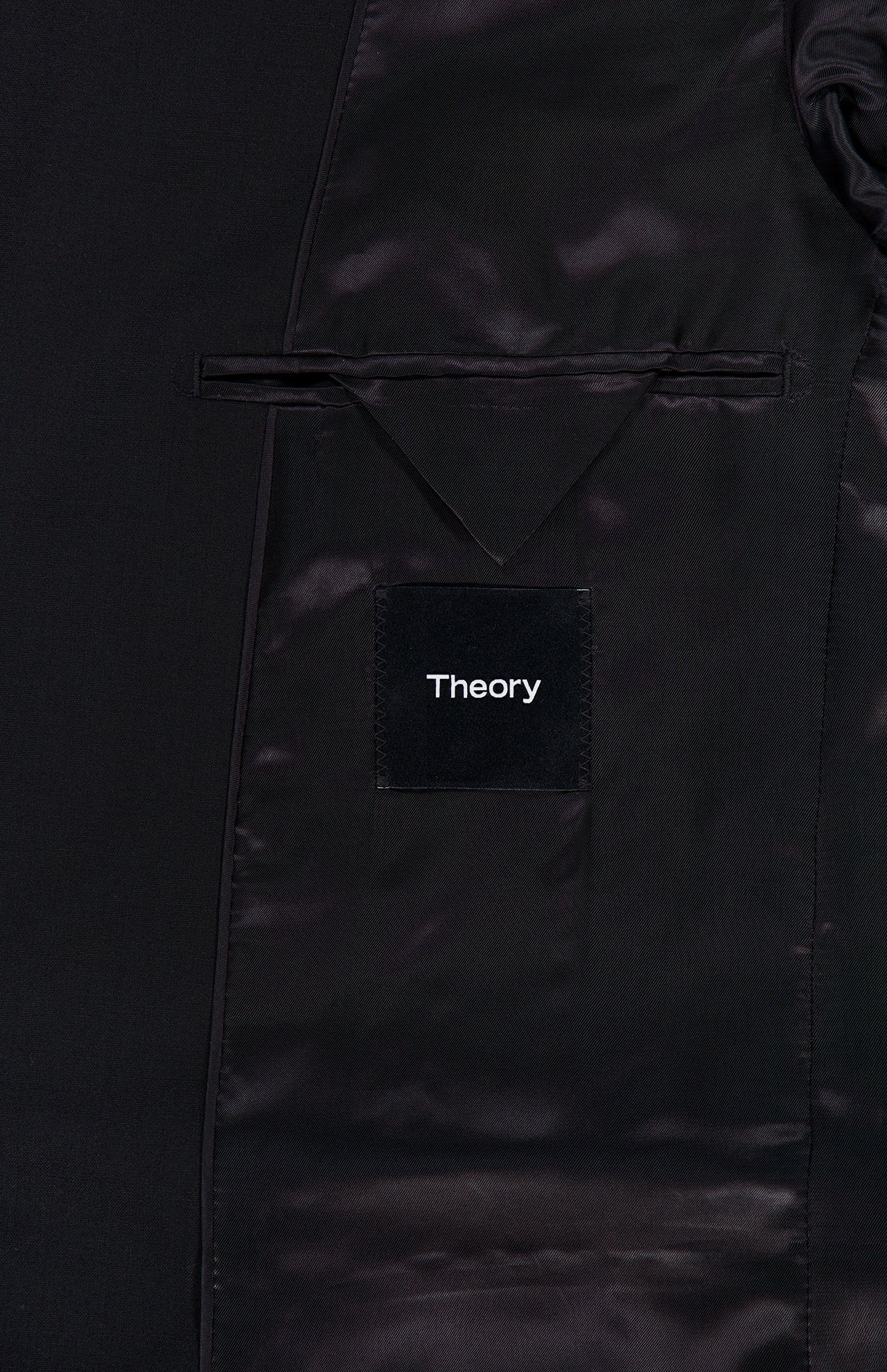 Close-up of the inside of the Chambers Blazer in Stretch Wool by THEORY, revealing a satin lining, an inner pocket with a flap, and a black label with THEORY stitched in white text. This wool sportcoat features refined tailoring and premium details for a polished finish.