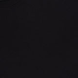 Close-up of the black textured fabric of the THEORY Delroy Cotton-blend T-Shirt, featuring a visible curved seam or collar in the upper left corner. The material is a double pique jersey, commonly chosen for its subtle texture and stretch—ideal for premium black t-shirts like this one.