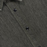Close-up of the THEORY Denim Snap-front Overshirt in olive green, styled as a collared button-up with black snap buttons and a visible THEORY label inside the collar. Crafted from stretch-cotton denim, this lightweight jacket delivers comfort and modern style.