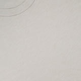 Close-up of the Essential Cosmo T-shirt by THEORY—a plain, lightweight light grey or off-white jersey tee with a round neckline and a visible black THEORY label in the top left corner. Made in Peru.