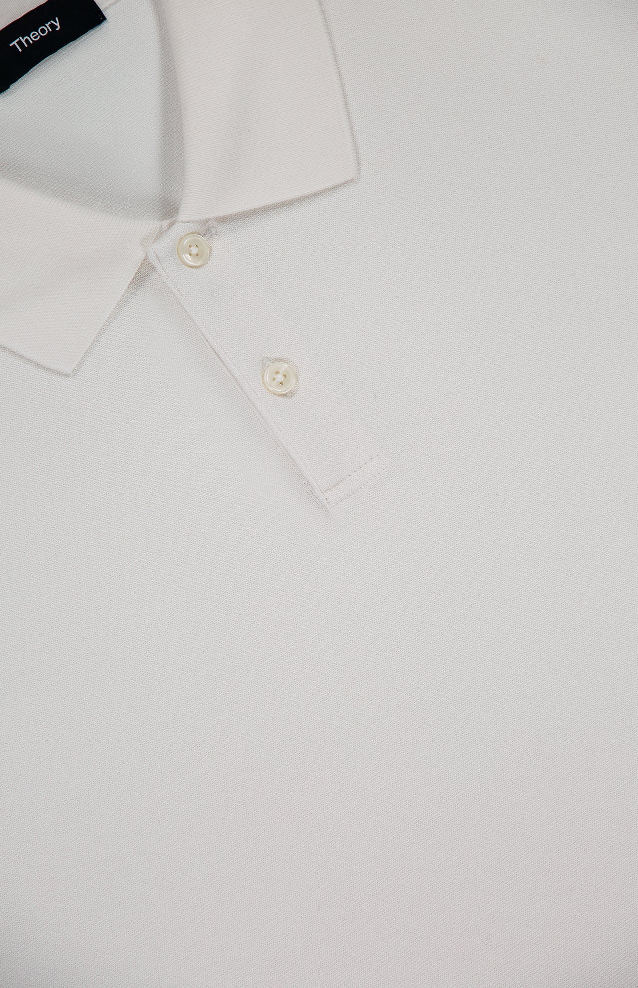 A close-up of the Goris Long Sleeve Polo Shirt by THEORY shows its white collared design with two buttons and a visible THEORY label at the neckline.