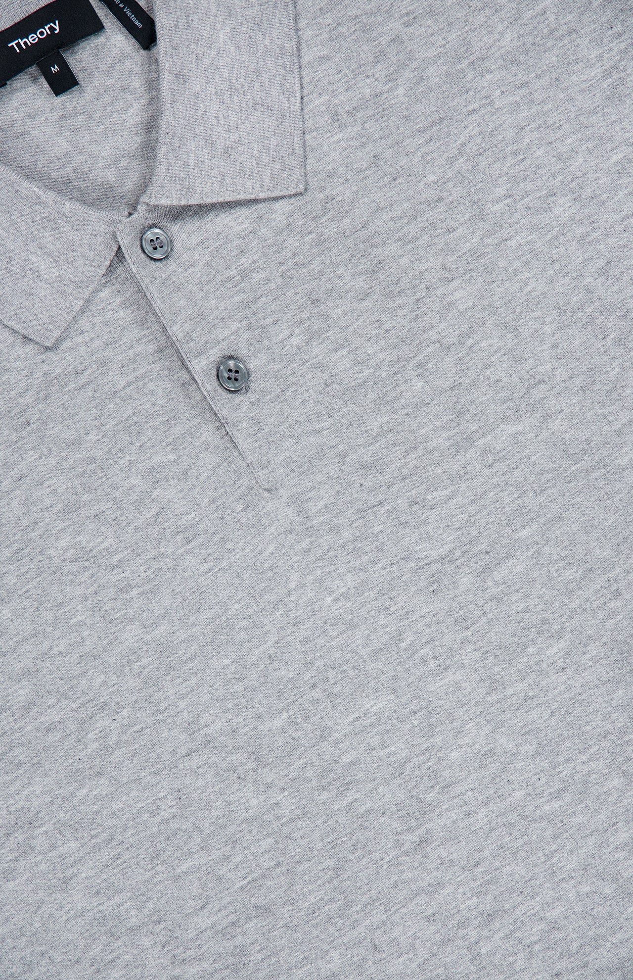 Close-up of the THEORY Goris Long Sleeve Polo Sweater in light gray, featuring a classic collar with two buttons. The soft knit fabric gives it a sweater-like appearance, and a black THEORY label with white text is partially visible at the neckline.
