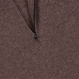 Close-up of the THEORY Hilles Cashmere Quarter Zip Sweater in brown, crafted from luxurious cashmere with a half-zip neckline and ribbed collar. The zipper is partially open, showing a black clothing tag inside. The fabric looks soft and textured, embodying the refined comfort that defines this premium cashmere quarter-zip sweater.