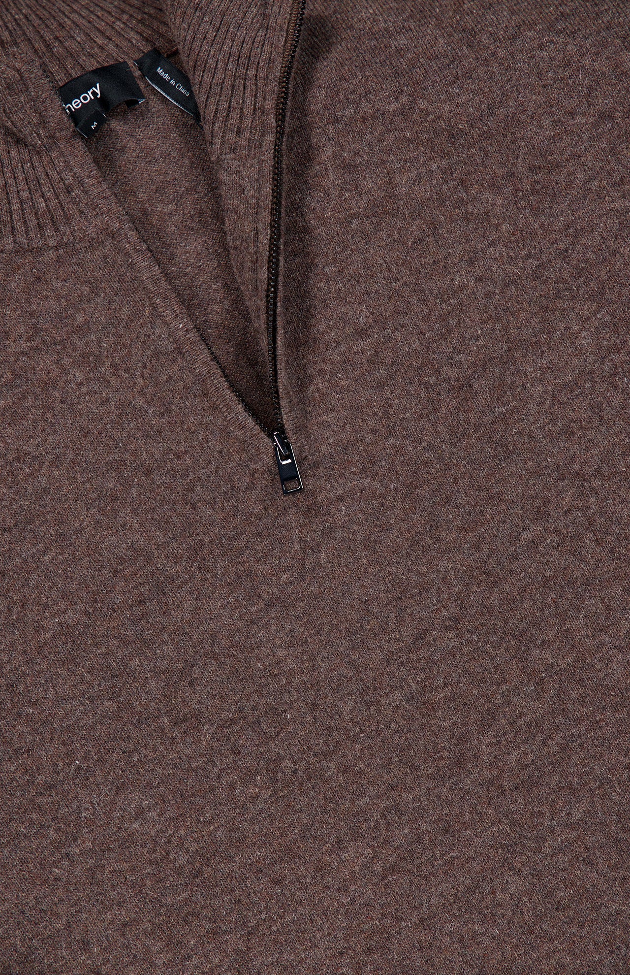 Close-up of the THEORY Hilles Cashmere Quarter Zip Sweater in brown, crafted from luxurious cashmere with a half-zip neckline and ribbed collar. The zipper is partially open, showing a black clothing tag inside. The fabric looks soft and textured, embodying the refined comfort that defines this premium cashmere quarter-zip sweater.
