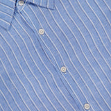 Close-up of the THEORY Irving Relaxed Linen Shirt in light blue with white vertical stripes, featuring a spread collar, white buttons, a relaxed fit, and a visible black THEORY label.