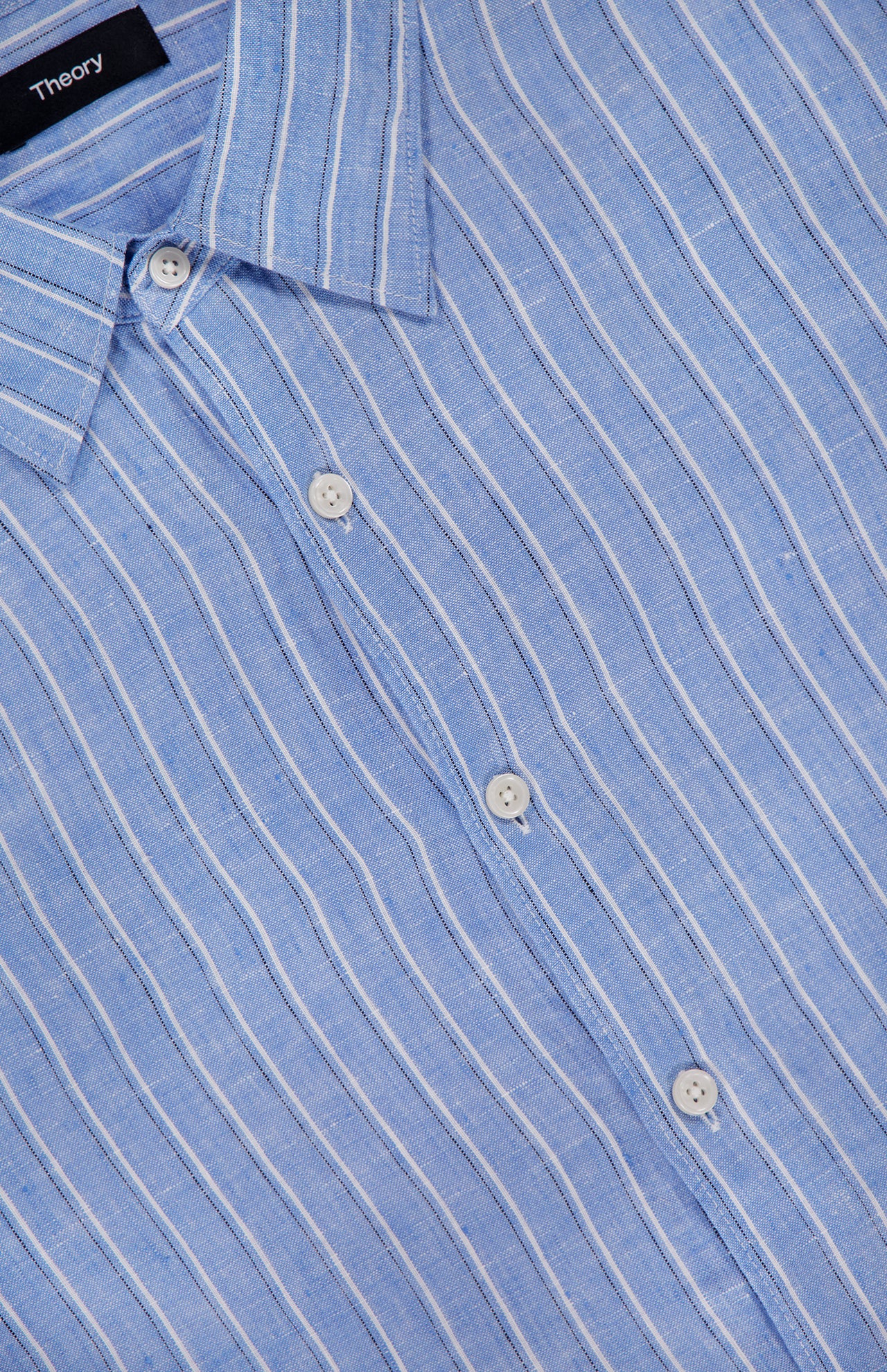 Close-up of the THEORY Irving Relaxed Linen Shirt in light blue with white vertical stripes, featuring a spread collar, white buttons, a relaxed fit, and a visible black THEORY label.