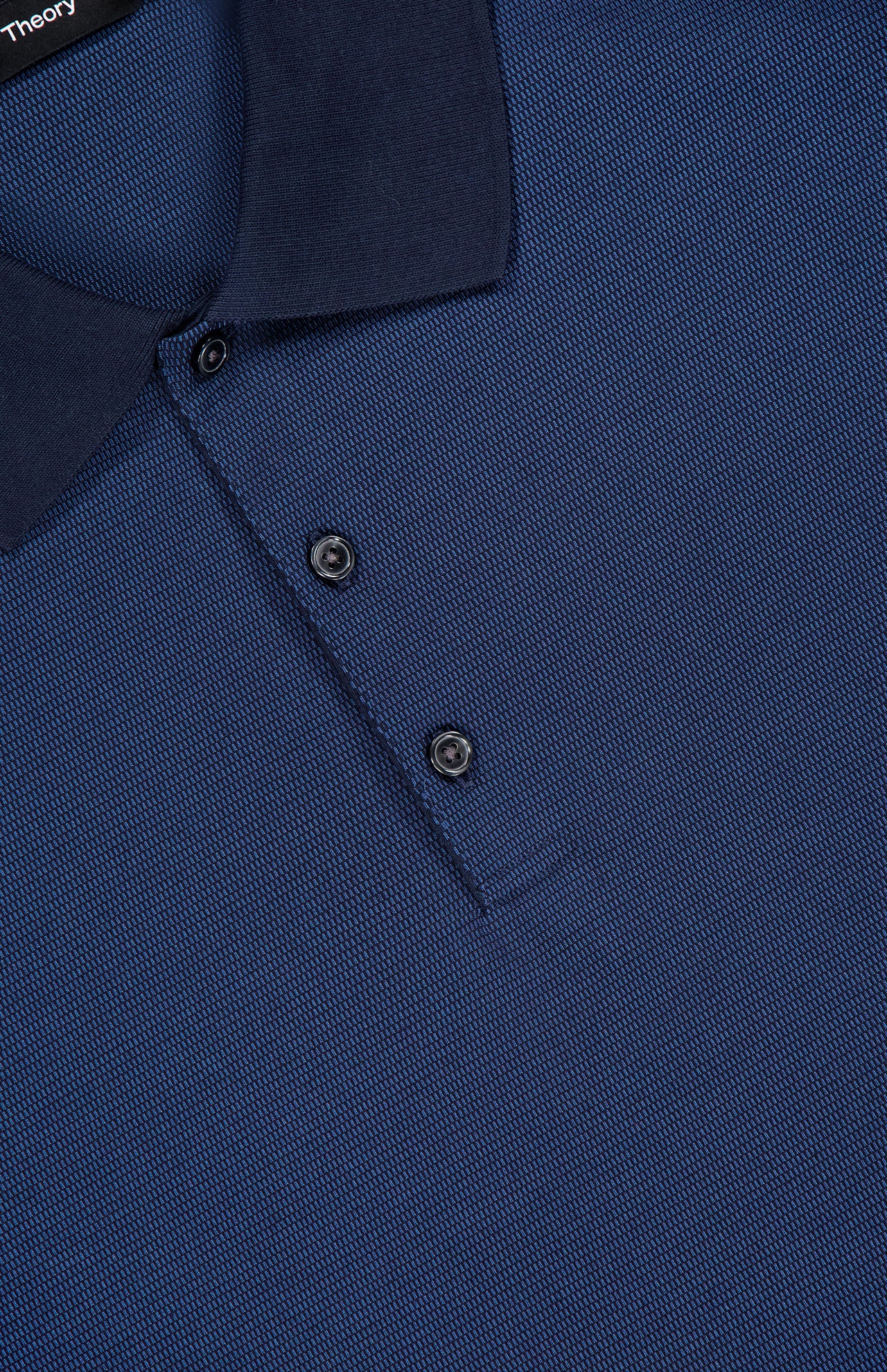 Close-up of the Jacquard Geo Polo Shirt by THEORY, a textured cotton navy blue slim fit polo featuring a subtle geometric pattern, dark collar, two black buttons, and "THEORY" partially visible on the collar tag.