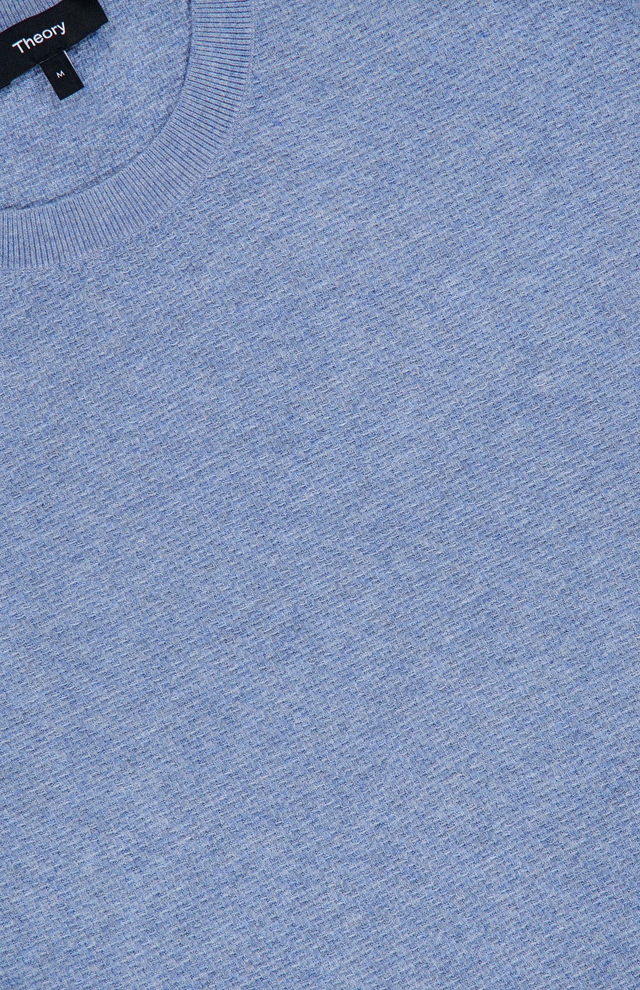 A close-up of the THEORY Riland Crewneck Sweater in light blue, crafted from a breathable knit material, featuring a ribbed crew neckline and a visible black THEORY brand label at the collar.