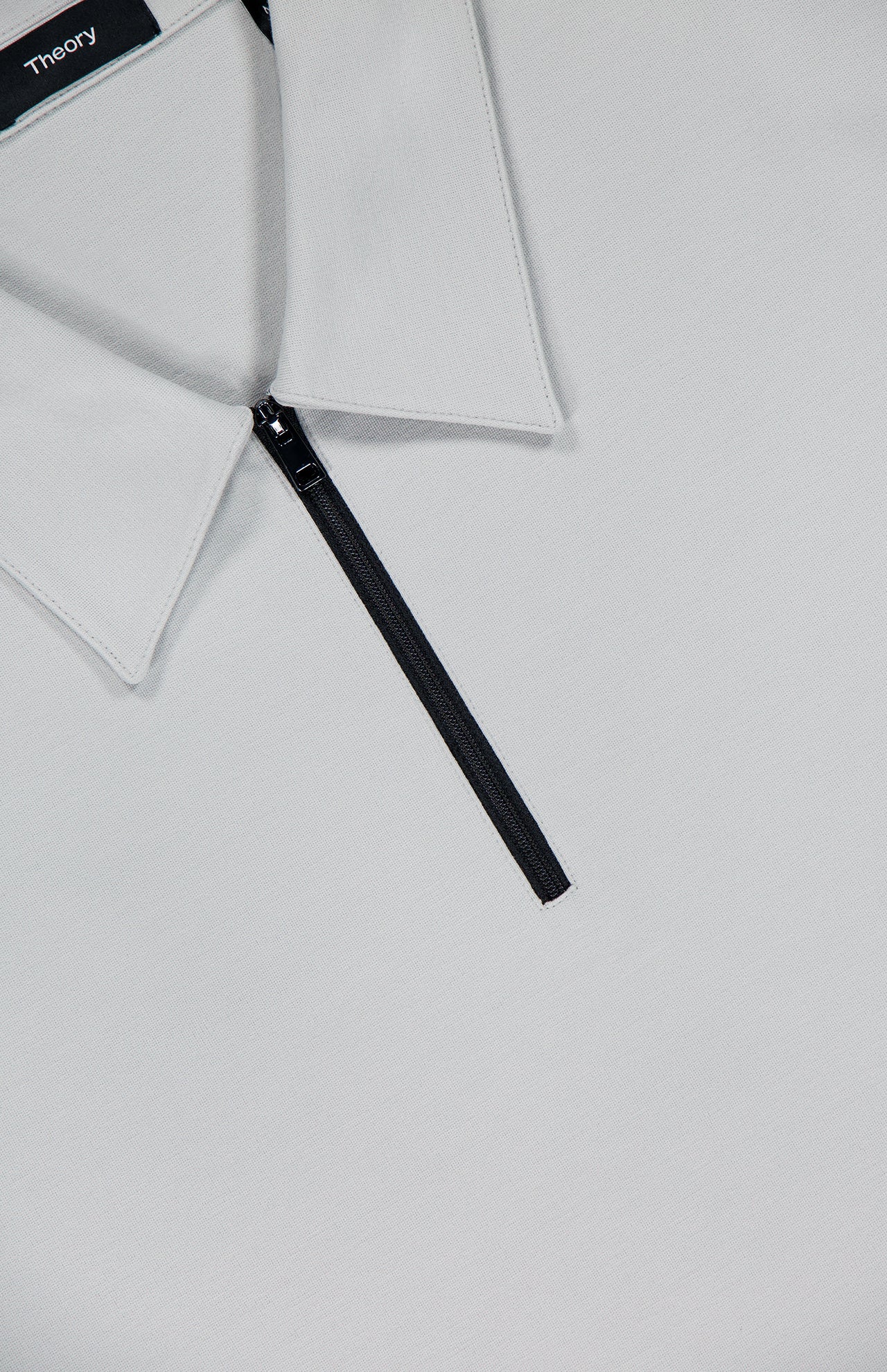 Close-up of the Ryder 1/4 Zip Polo Shirt by THEORY in light gray viscose-blend jersey, featuring a rib-knit collar and a black quarter zipper. The THEORY brand label is visible inside the collar.