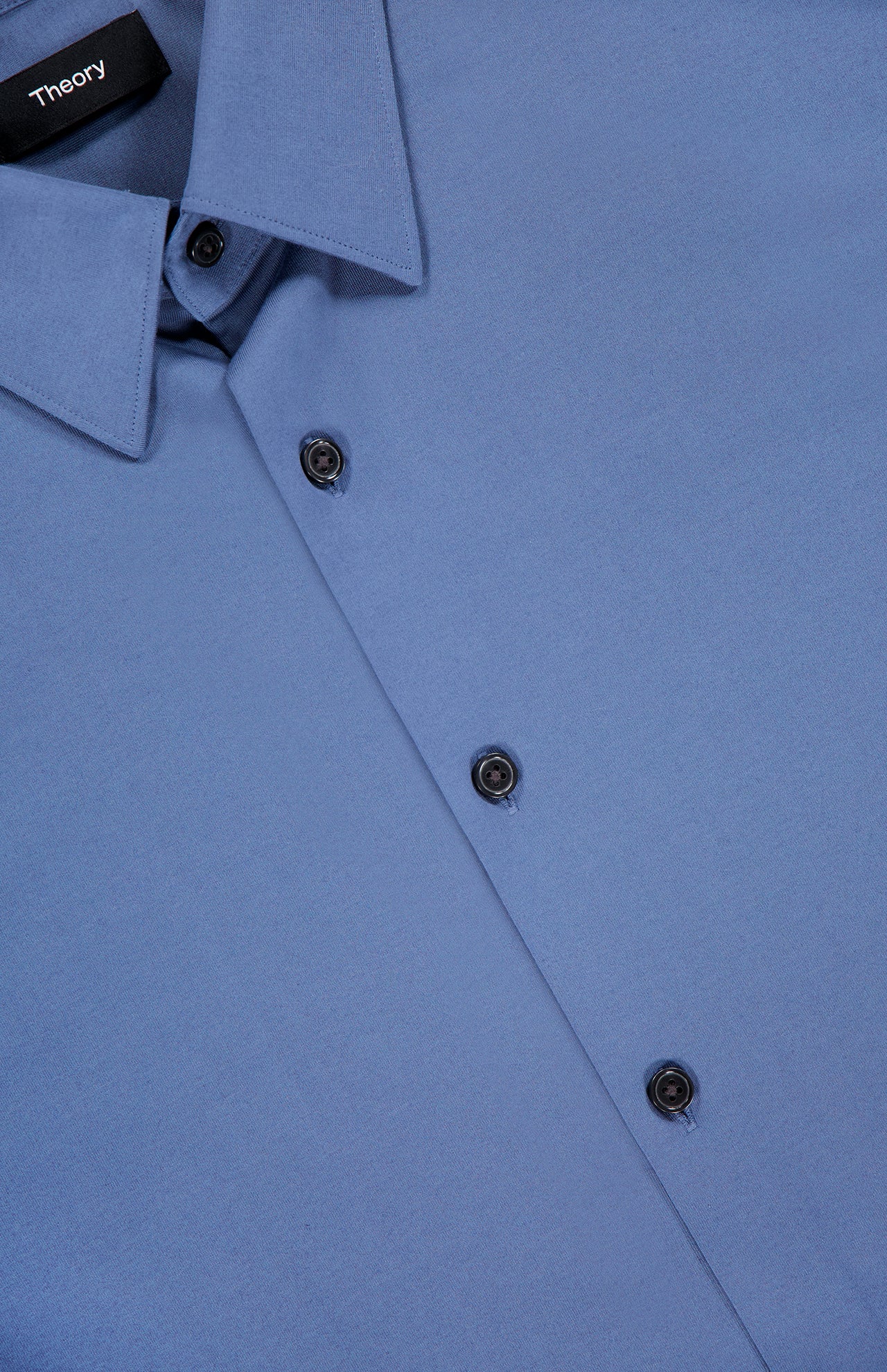 A close-up of the THEORY Sylvain Long Sleeve Structure Dress Shirt in blue shows its slim fit, collar, and black buttons, with a THEORY brand tag on the inside collar.