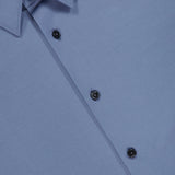 Close-up of a neatly buttoned, slim fit light blue Sylvain Structure Dress Shirt with black buttons and a pointed collar. The THEORY brand label is visible inside the collar, emphasizing the shirt’s modern silhouette and wrinkle-resistant fabric.