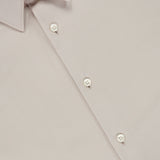 A close-up of the Sylvain Structure Dress Shirt by THEORY in light beige showcases its pointed collar, four white buttons, and a prominent black tag featuring the THEORY logo in white text. This dress shirt is wrinkle-resistant, machine-washable, and expertly blends classic design with easy care.