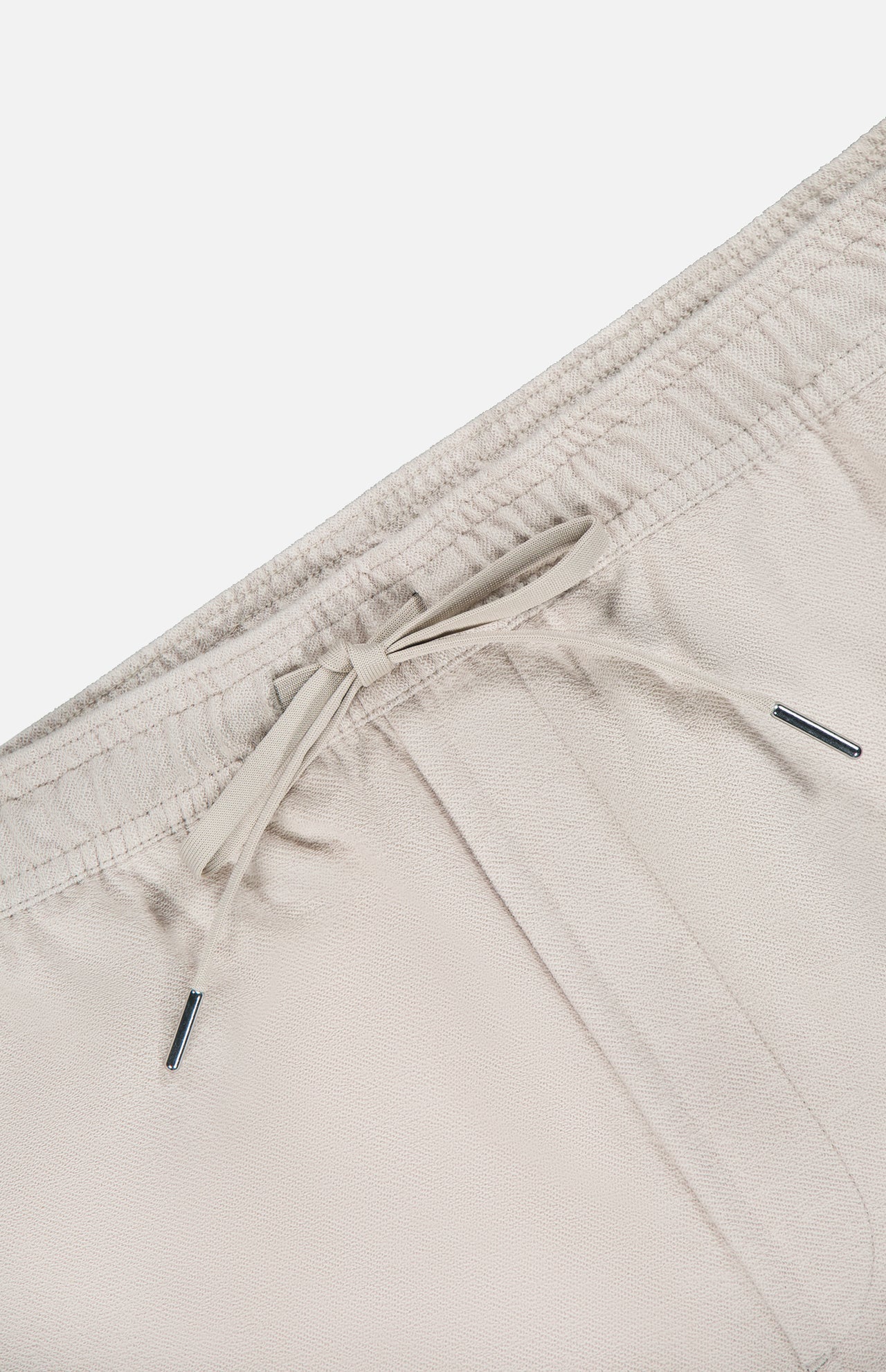 Close-up of the waistband of THEORY Terry Drawstring Shorts in light beige, featuring an elastic band and adjustable drawstring with metal tips, shown against a plain white background.