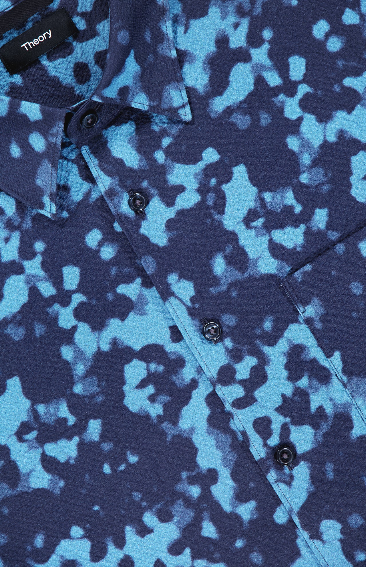 Close-up of the THEORY Weekend Short Sleeve Shirt, featuring a blue and black abstract splash pattern, black buttons, a chest pocket, and a cotton-blend fabric.