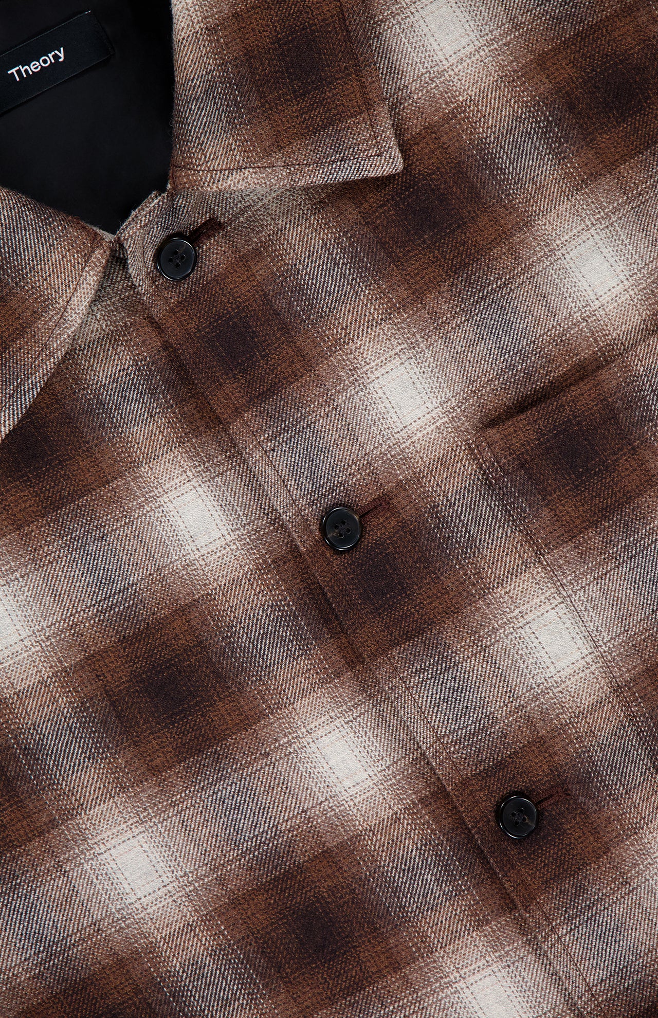 Close-up of the THEORY Wool Plaid Button Down Shirt, featuring brown and beige plaid fabric, black buttons, and a visible brand label at the collar.