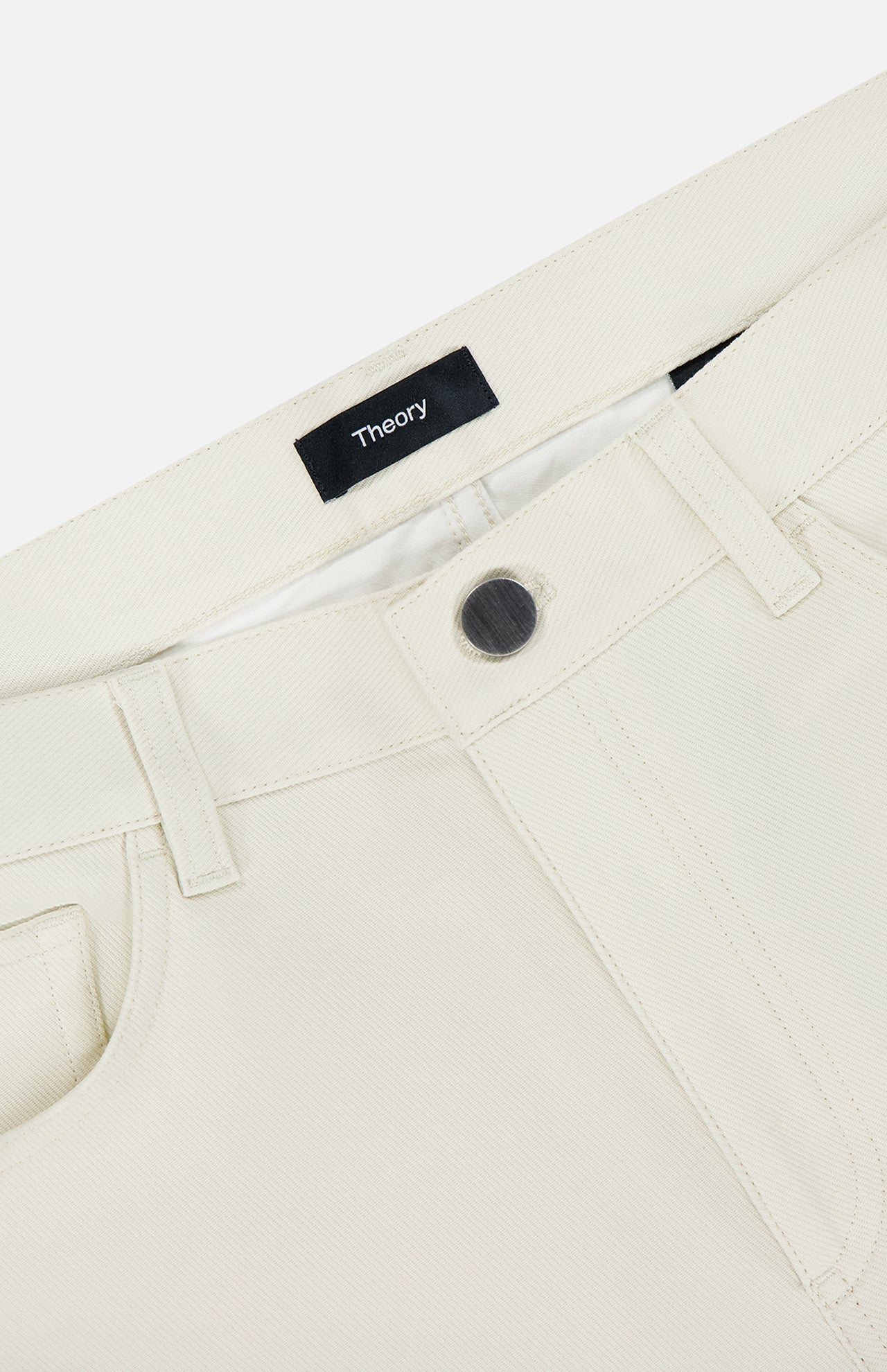 Close-up of the waistband on Raffi Stretch Twill Pants in an oat milk tone, featuring a black button, belt loops, front pocket, and a black THEORY label sewn inside.
