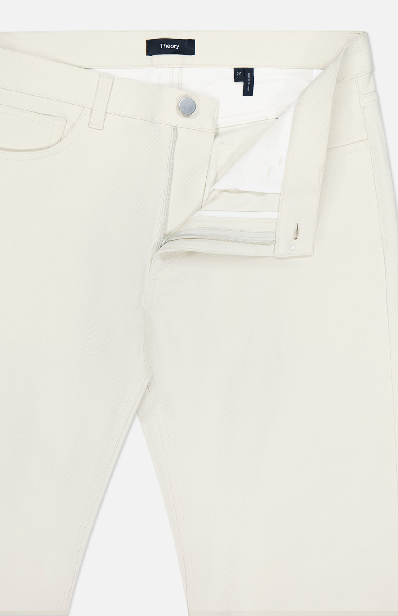 The THEORY Raffi Stretch Twill Pants in oat milk feature a slim fit, visible zipper, button closure, front pocket, and belt loops, shown partially unzipped to highlight the interior waistband and label.