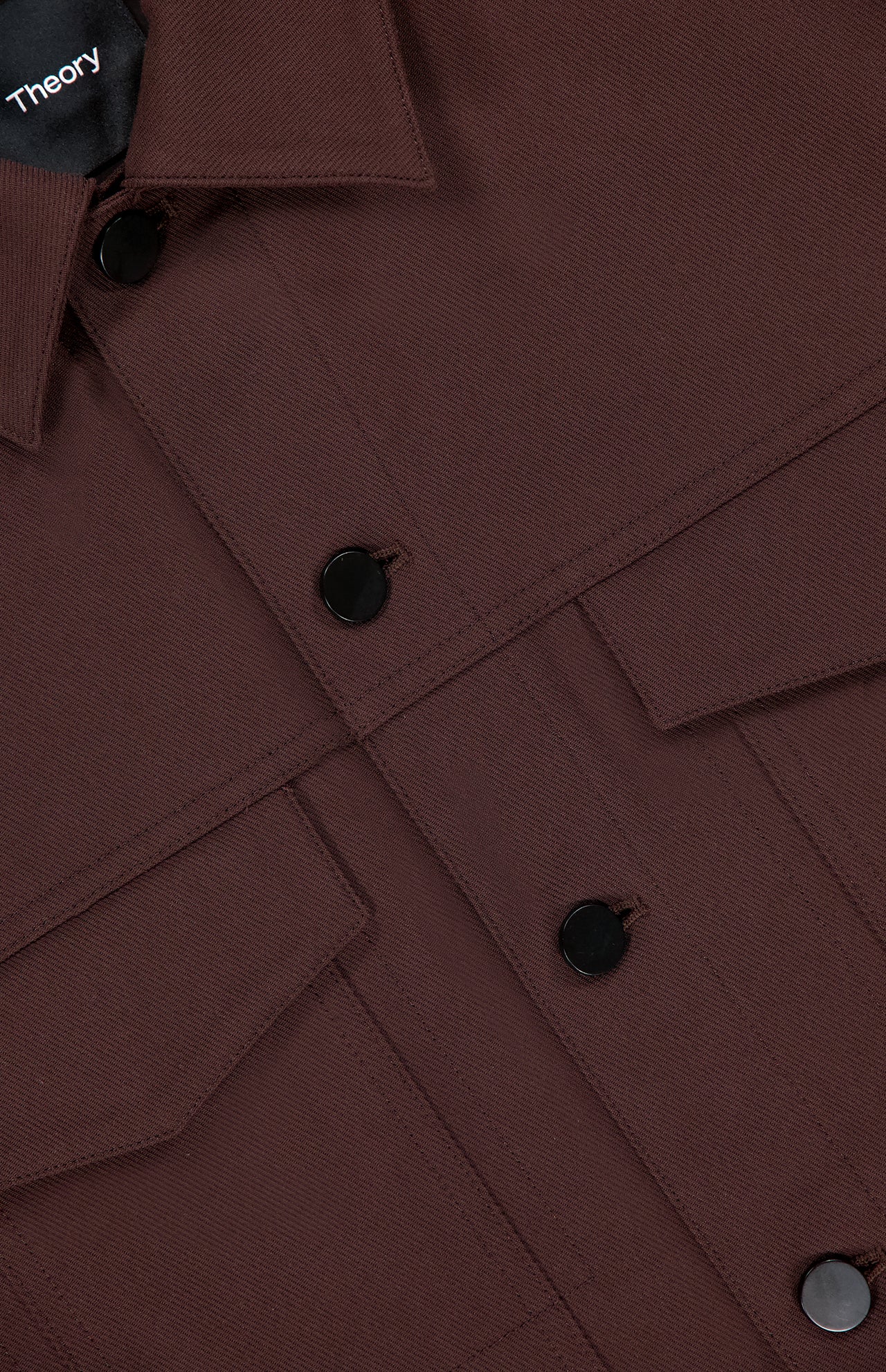 Close-up of the River Twill Trucker Jacket by THEORY, featuring black buttons, two flap chest pockets, and a visible collar. Made from textured twill performance fabric for breathability and comfort.