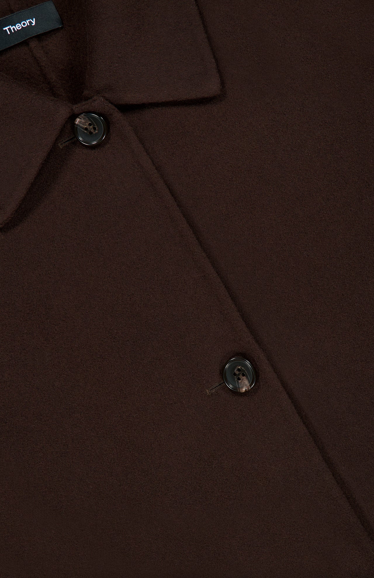 Close-up of the Boxy Cuff Jacket by THEORY in chocolate brown wool-blend, featuring two dark buttons, a pointed collar, and part of a black label with white text. The soft, smooth fabric hints at the jacket’s modern boxy fit and stylish design.
