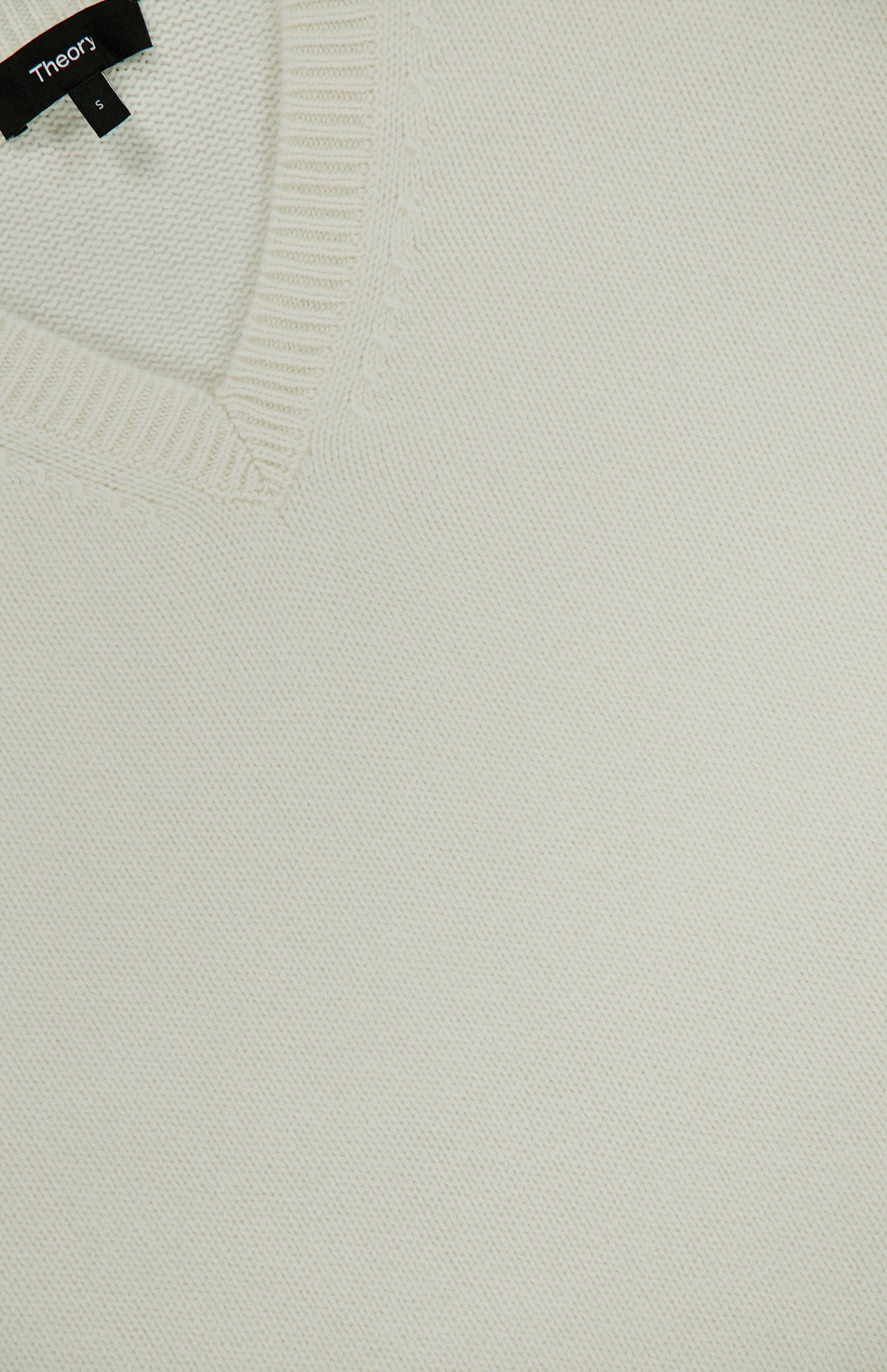 Close-up of the Cashmere Cropped V-Neck T-Shirt in ivory, featuring a cream-colored ribbed V-neck collar. A black THEORY brand tag with size S is visible at the neckline.
