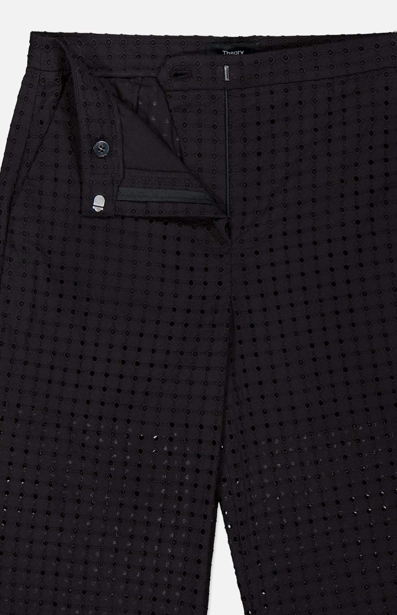 Close-up of THEORY’s Easy Eyelet Slim Fit Pant in black embroidered eyelet cotton with circular cutouts, shown partially unzipped to reveal the waistband, button, and lining. The slim fit style is displayed flat.