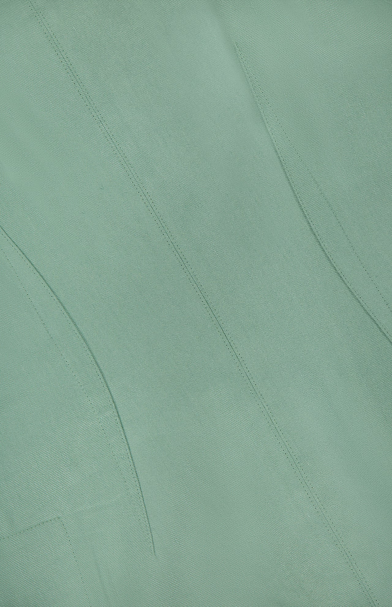 Close-up of the THEORY Linen Apron Mini Dress in sage green, featuring visible stitching and seams that form curved and straight lines across the textured fabric.