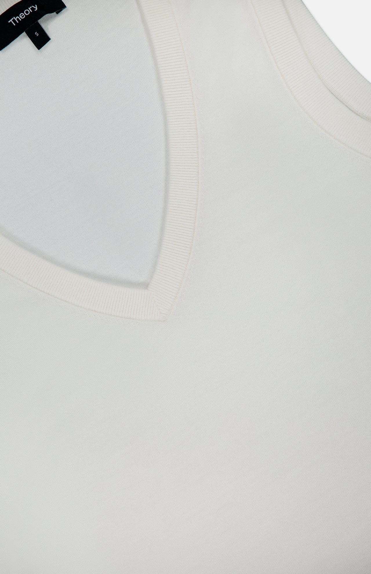 Close-up of a white Merino Slim Tank Top by THEORY, featuring ribbed edging on the neckline and armholes. A black THEORY tag is visible at the top left.