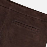 Close-up of the THEORY Lamb Leather Mini Trouser Skirt in chocolate brown shows a welt pocket accentuating the skirt’s clean, minimal design on a smooth leather surface. The fabric displays a rich, soft texture with visible stitching detail near the upper edge.