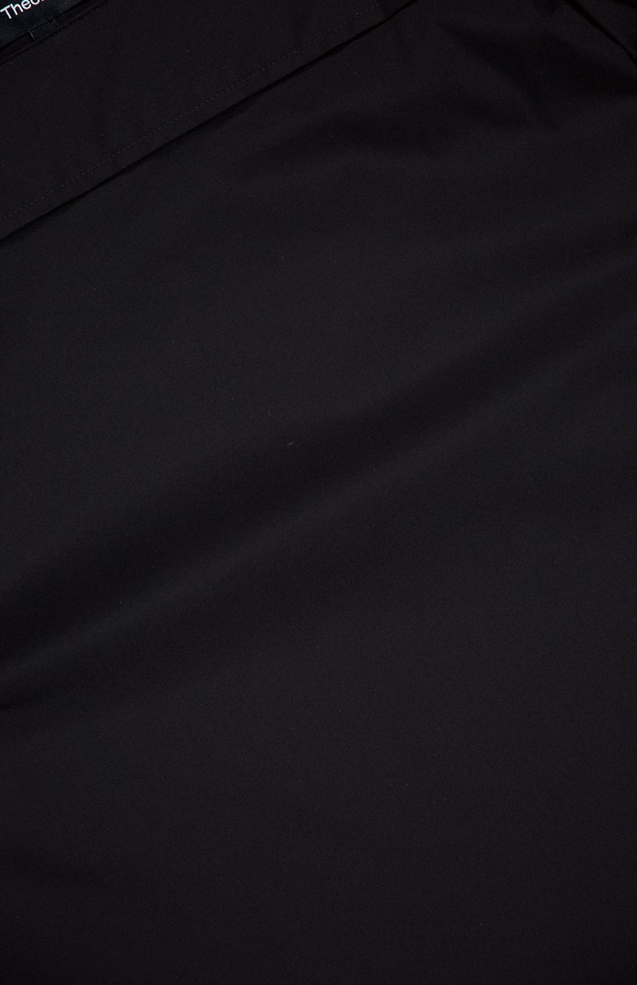 A close-up of THEORY's Open Sleeve Boatneck Top in smooth black fabric, with subtle folds and a boat neck—embodying quiet luxury.