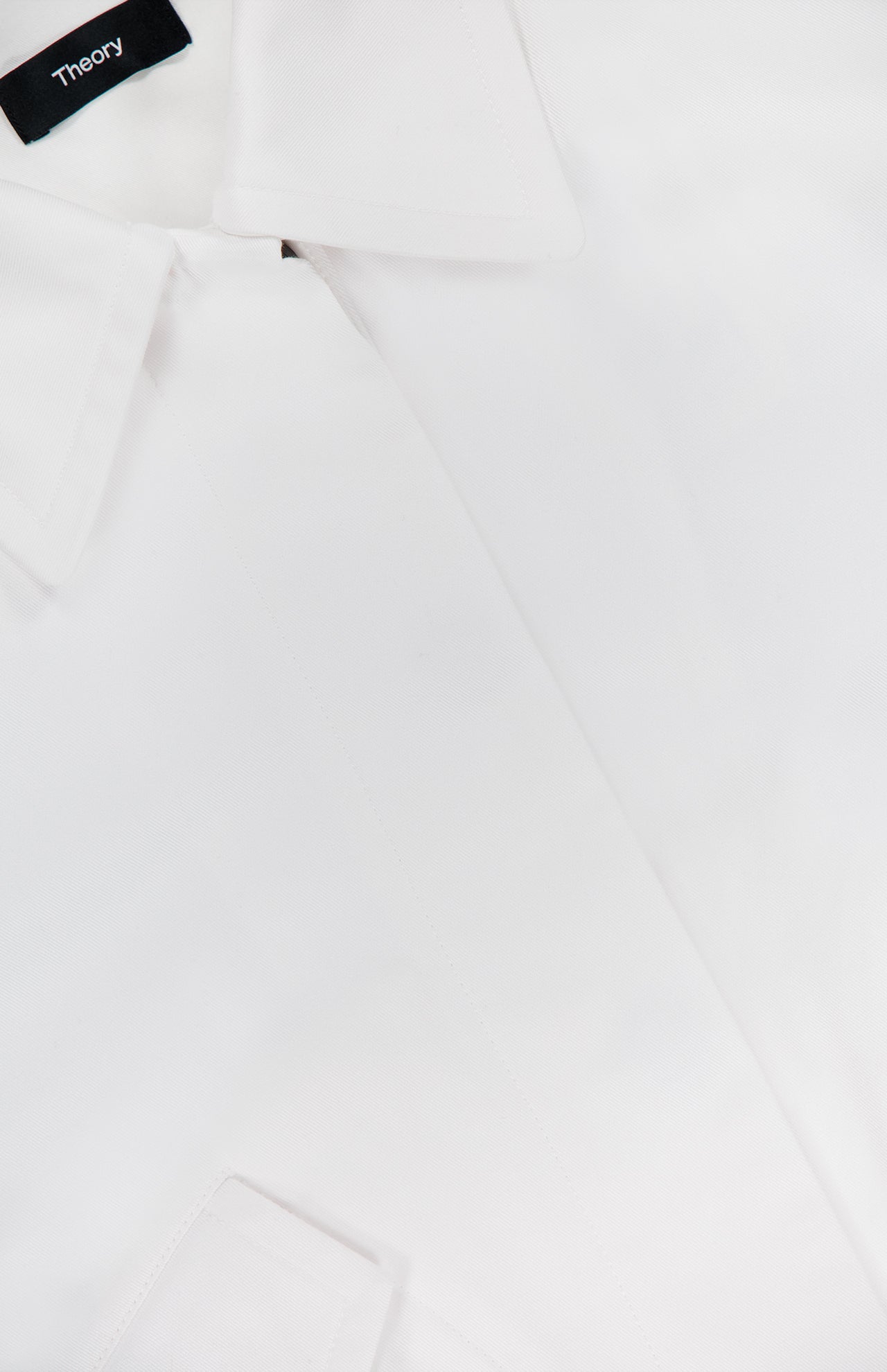 Close-up of the THEORY Relaxed Flyer Jacket, a white cotton-blend piece with crisp, smooth fabric. Features include a sharp collar and pocket flap, offering lightweight warmth and displaying the signature THEORY label.