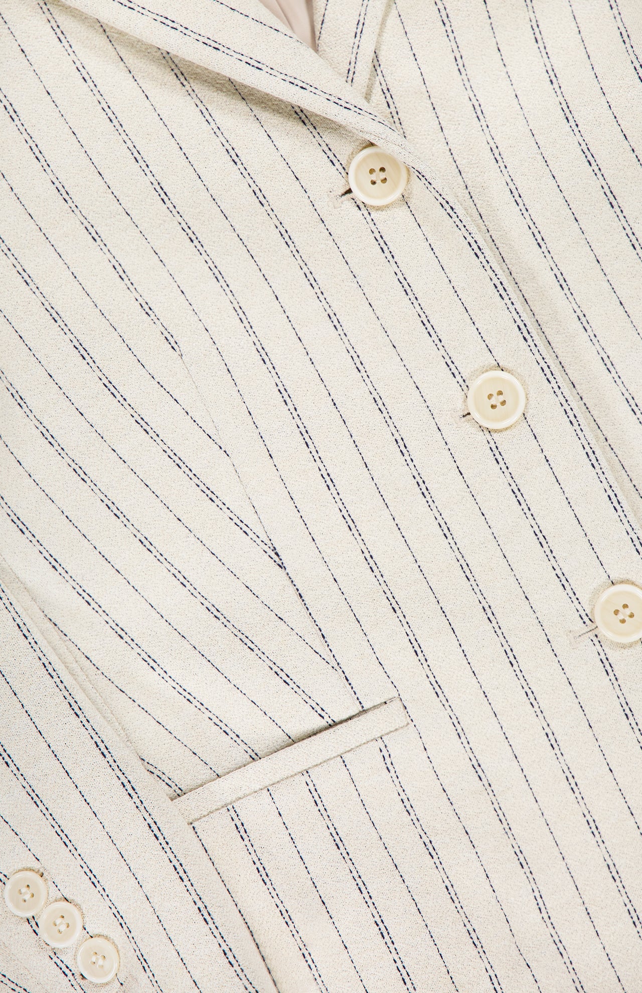Close-up of the THEORY Shrunken 3 Button Jacket in cream, featuring thin dark pinstripes, beige buttons, a front pocket, textured crepe fabric, and visible stitching.