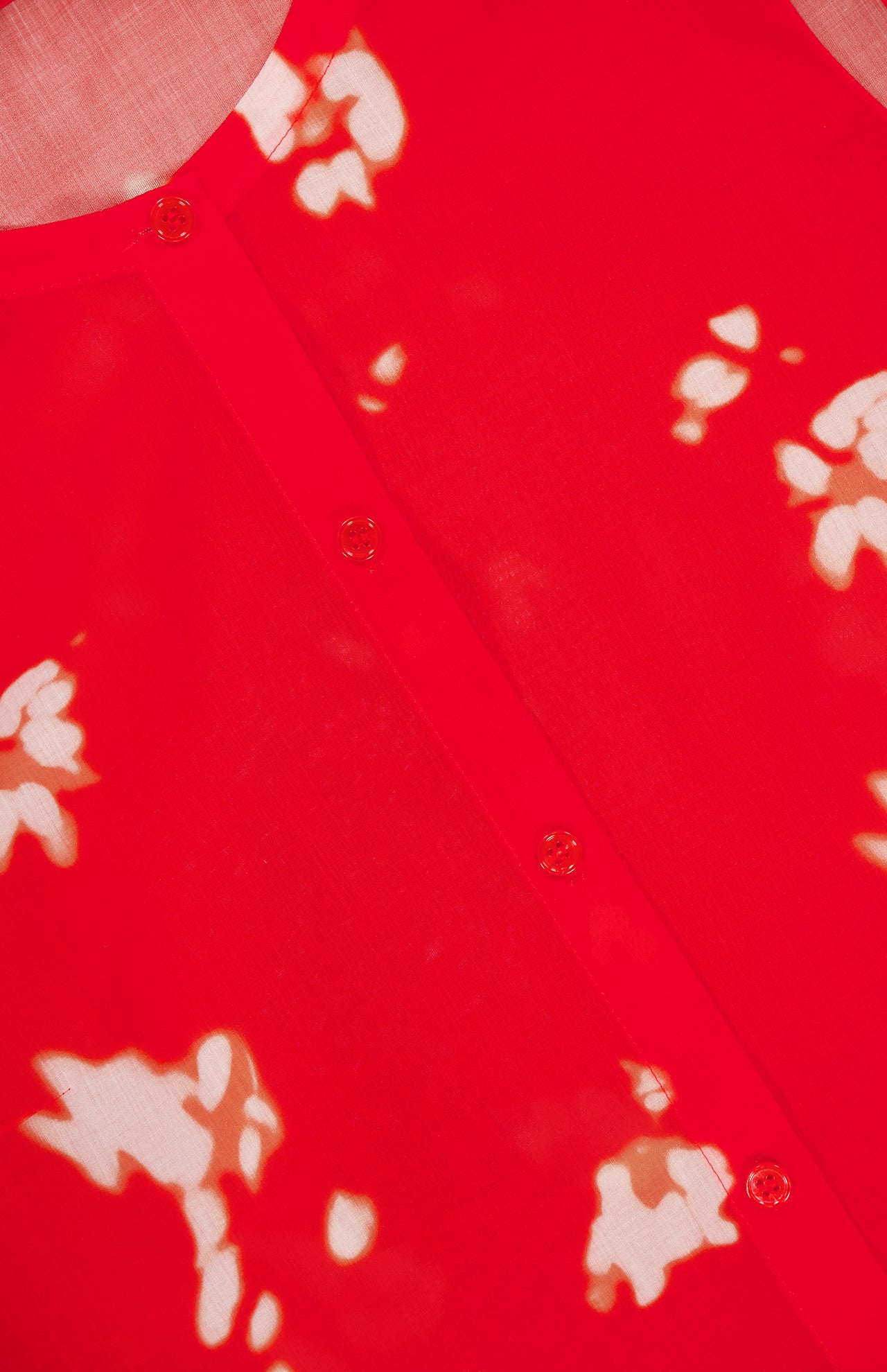 Close-up of the THEORY Sleeveless Abstract Floral Shell Top, featuring bright red fabric with white abstract floral patterns and a row of small, round buttons down the center. The material appears light and slightly sheer.